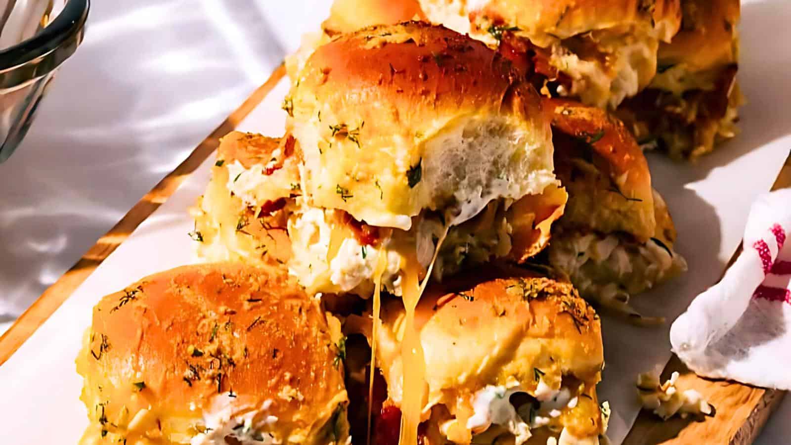 A pile of cheese-stuffed sliders with herbs and a golden-brown crust on a white serving platter.