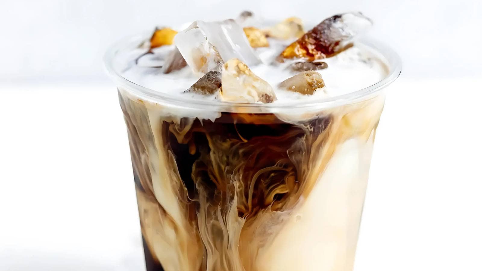 A cold coffee drink with swirls of cream and ice cubes in a clear plastic cup.