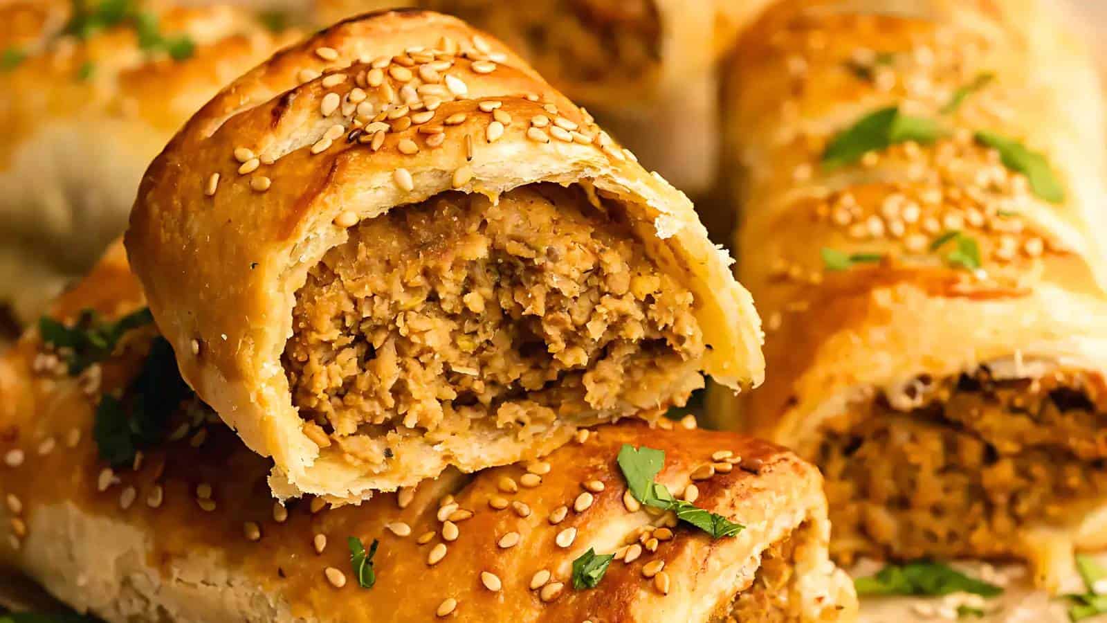 Sliced sausage rolls topped with sesame seeds, revealing a savory filling. Parsley in the background.
