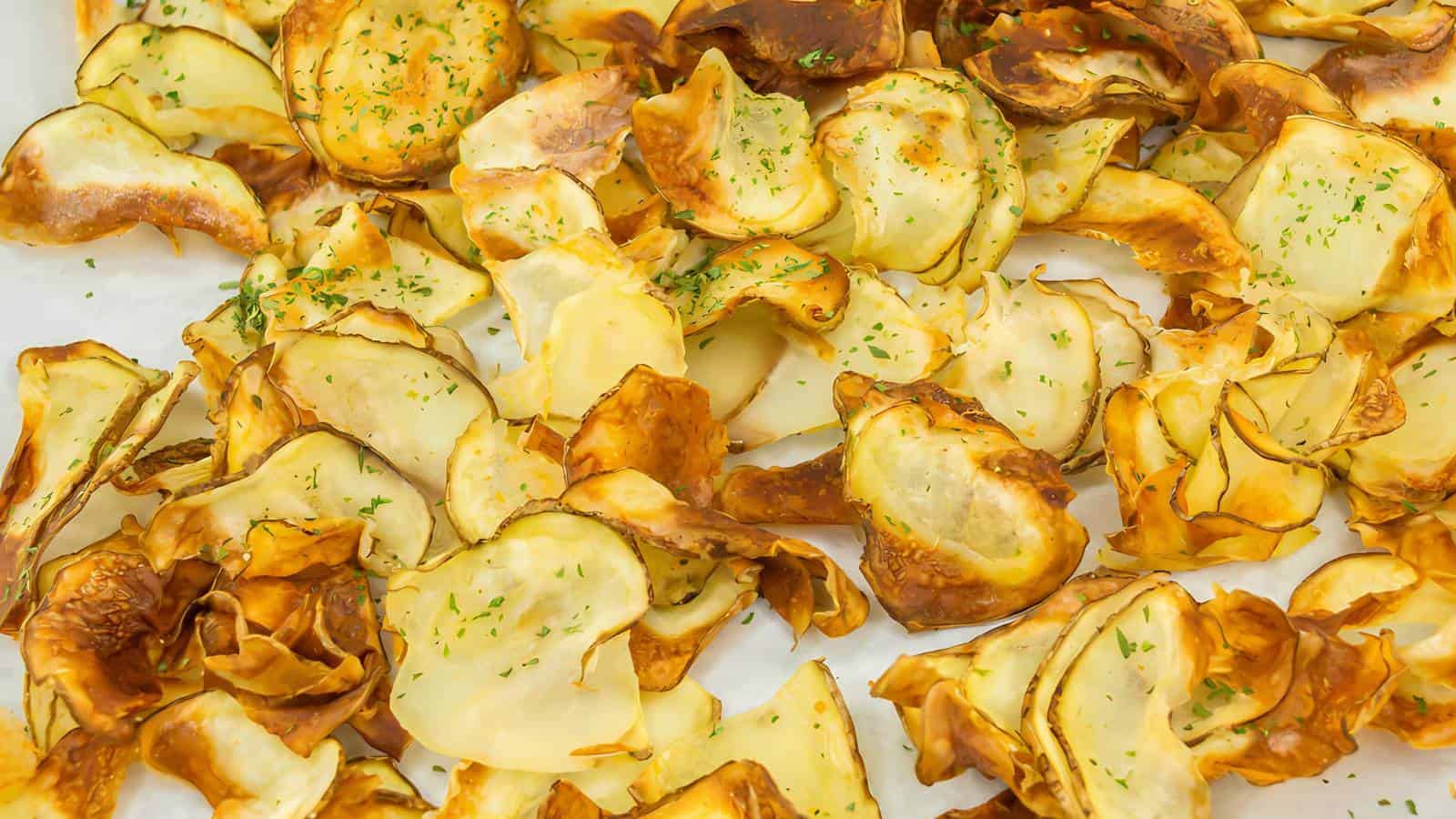A pile of thinly sliced, golden brown potato chips topped with green herbs.