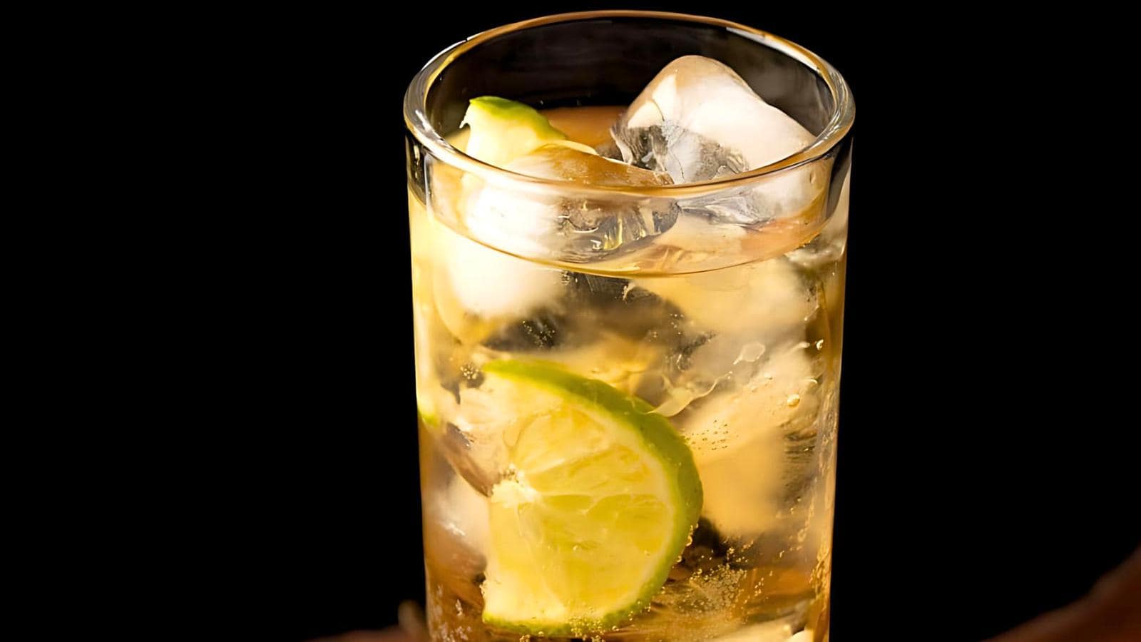 A tall glass filled with a light-colored liquid, ice cubes, and lime slices.