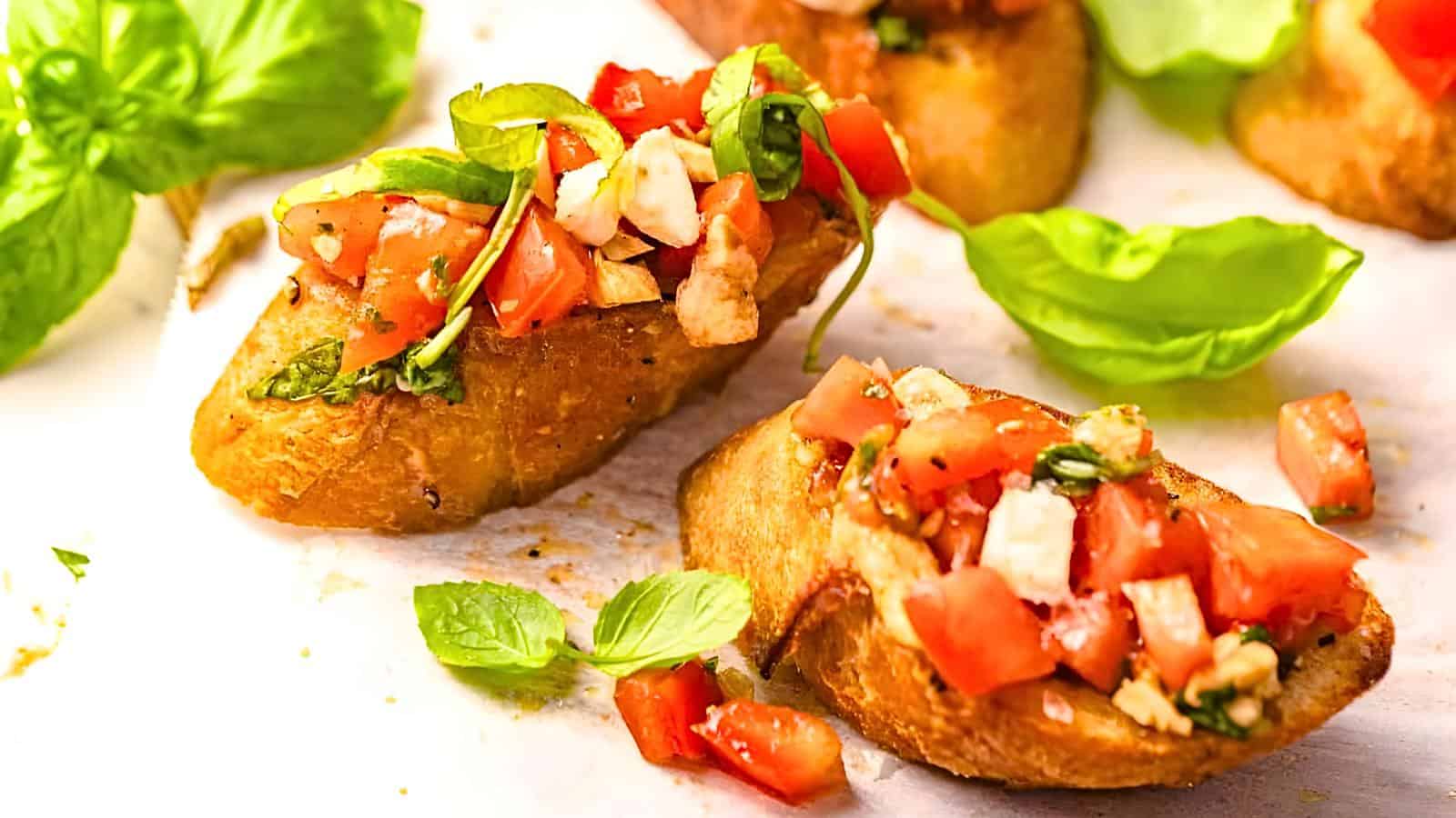 Diced tomatoes, basil leaves, and cheese on toasted bread slices arranged on a white surface with scattered basil leaves.