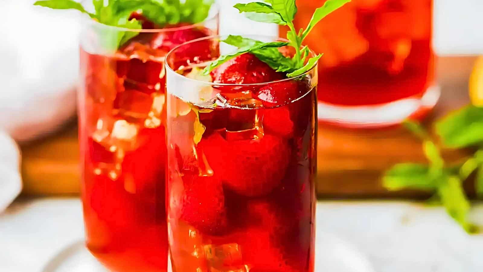 Tall glasses filled with a red beverage, garnished with strawberries and mint leaves, are displayed on a wooden tray.