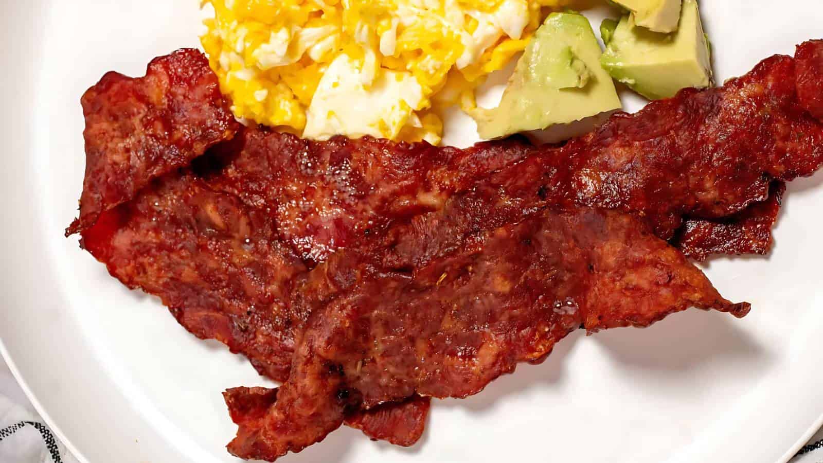 Crispy bacon strips, scrambled eggs, and avocado slices on a plate.