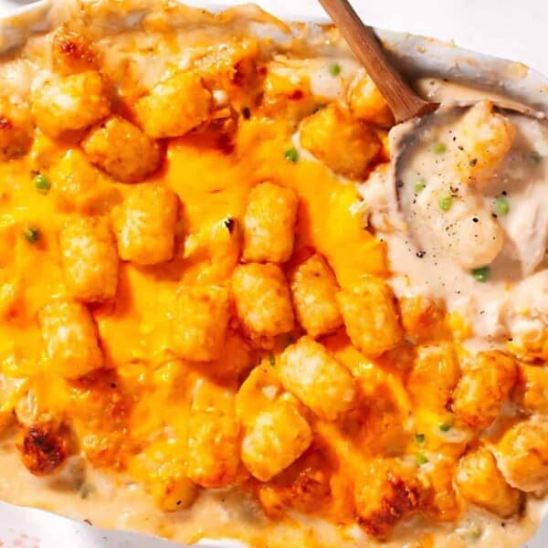A baked casserole dish filled with tater tots, melted cheese, and creamy sauce, with a wooden spoon placed on the right.