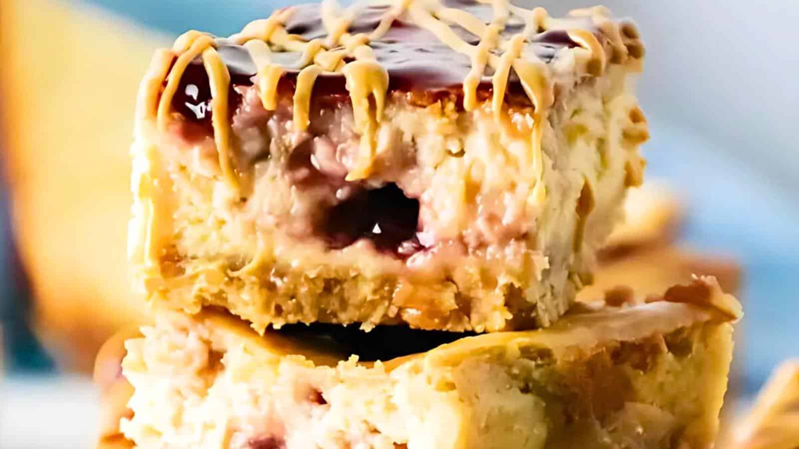 A close-up of stacked cookie bars with a creamy filling and a swirl of purple jam. The top is drizzled with a light brown sauce. The texture appears soft and gooey.