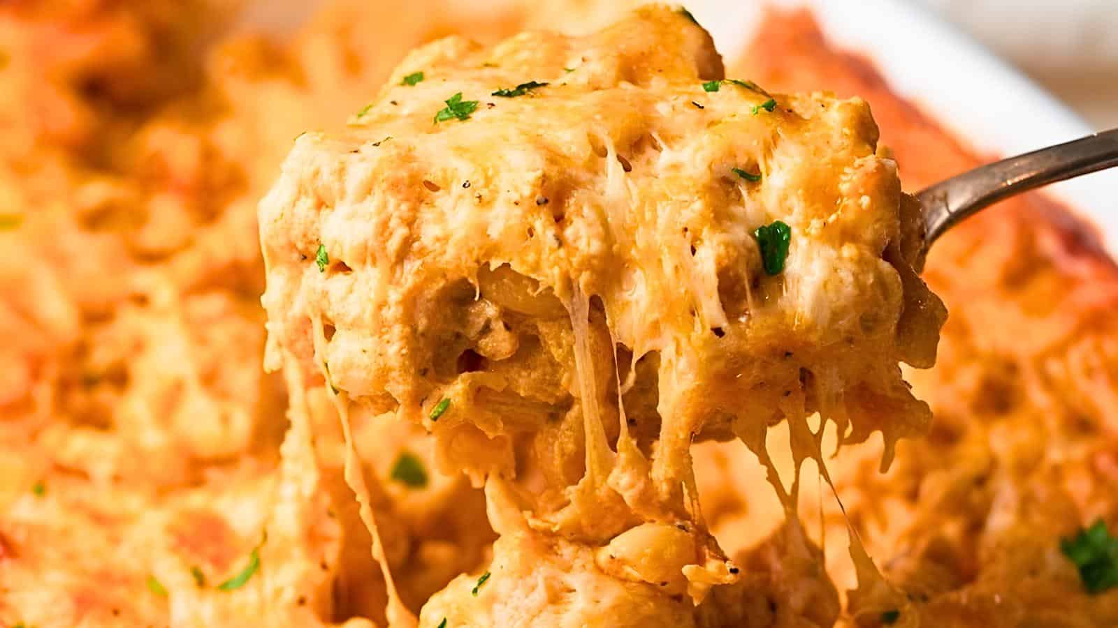 A spoon lifting a portion of cheesy baked casserole with melted cheese and garnished with herbs.