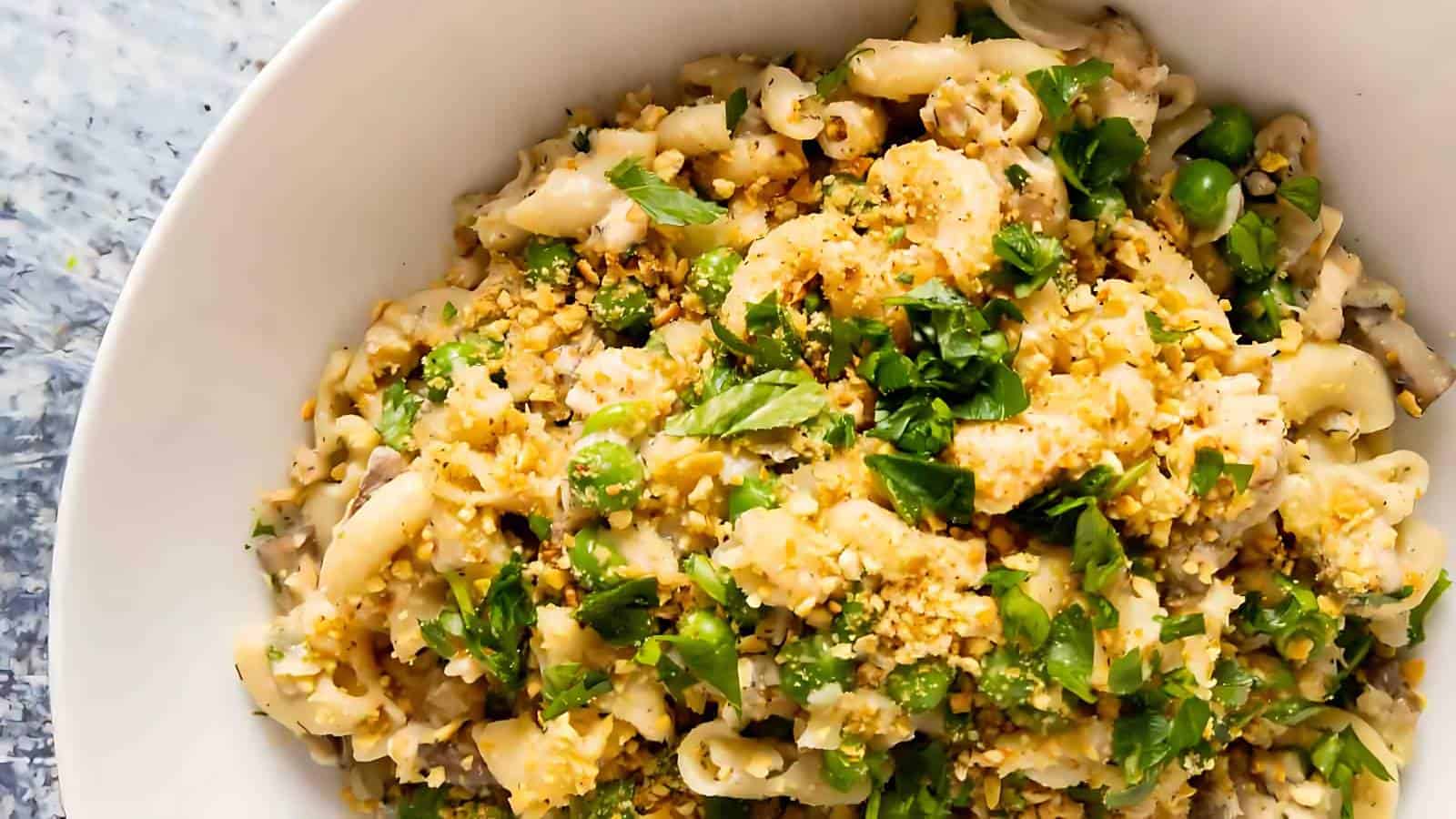 A bowl of pasta mixed with peas, topped with chopped herbs and breadcrumbs.