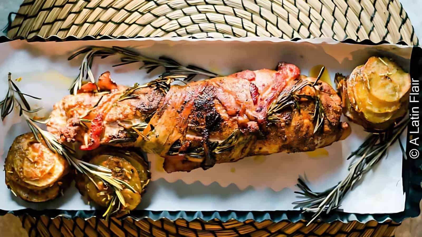 A roasted meat dish with rosemary garnish and potatoes, presented in a large rectangular serving dish.