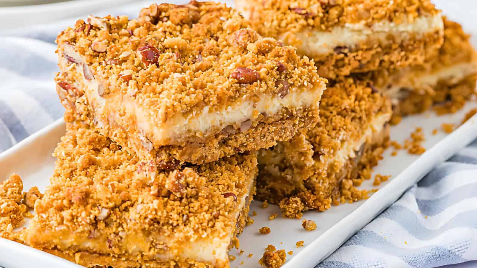 Several squares of crumbly dessert bars with a creamy filling, topped with a streusel-like layer, arranged on a white plate.