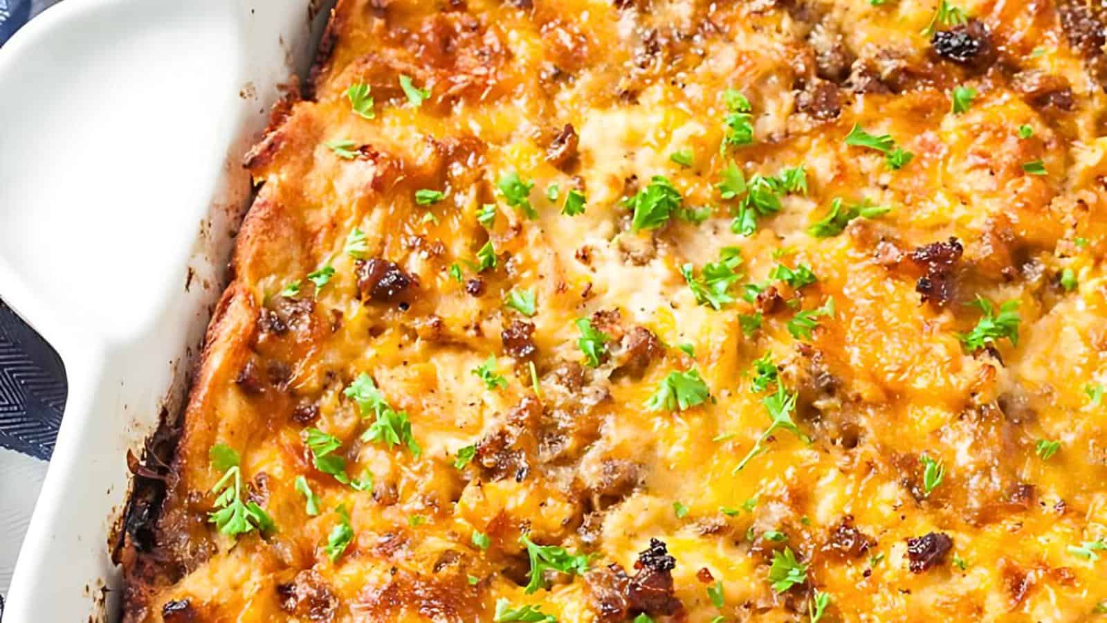 A white baking dish containing a baked casserole topped with melted cheese, small meat pieces, and garnished with fresh parsley.
