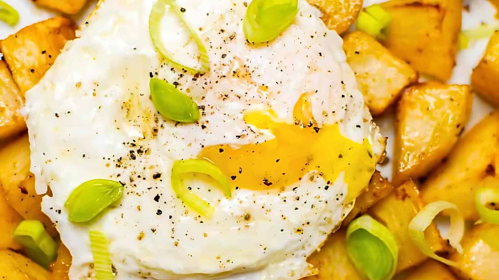 A fried egg with a partially runny yolk, garnished with chopped green onions, served over diced and seasoned potatoes.