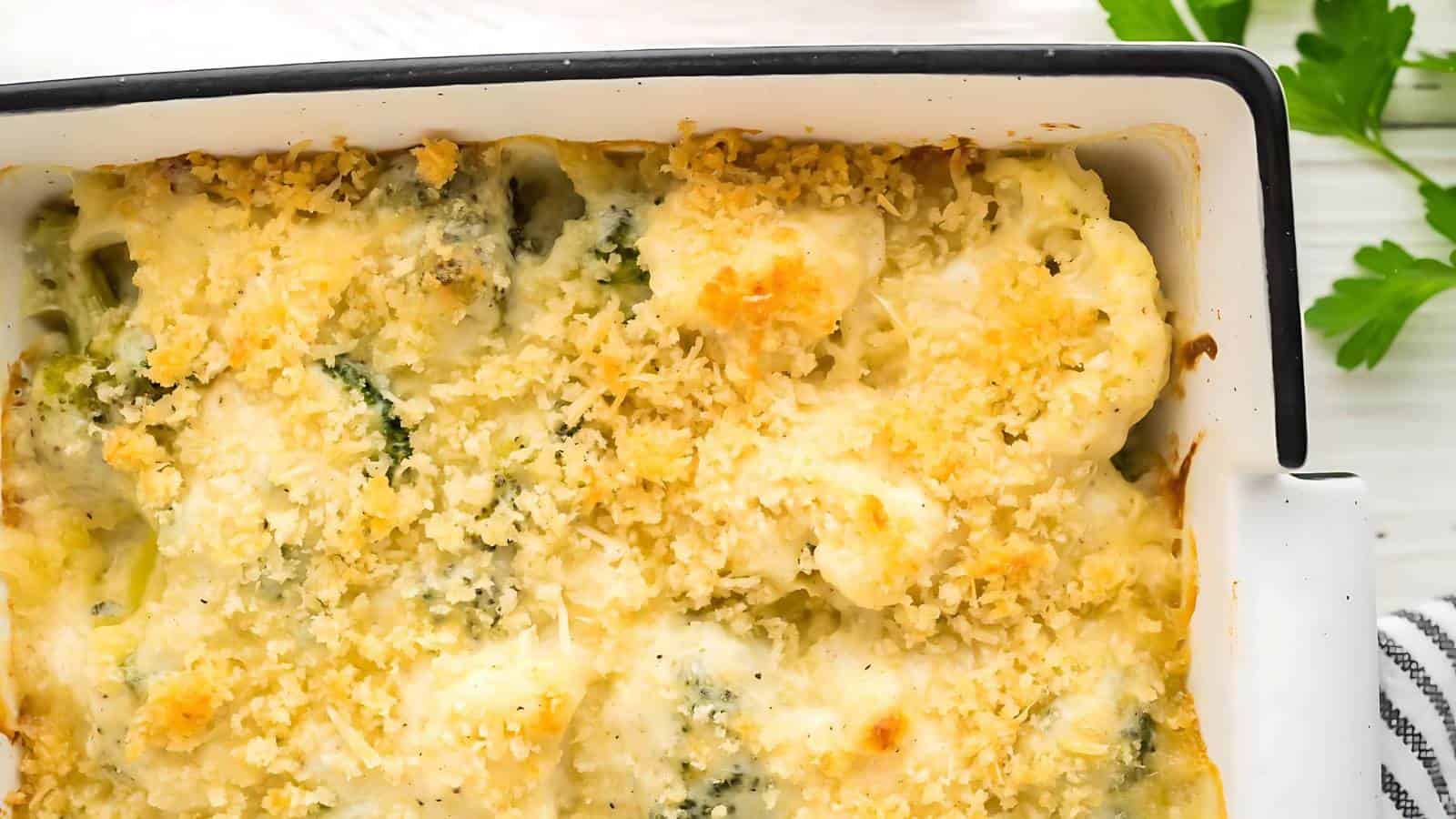 A close-up of baked cauliflower au gratin topped with a golden breadcrumb crust in a rectangular dish, with parsley garnish visible in the background.
