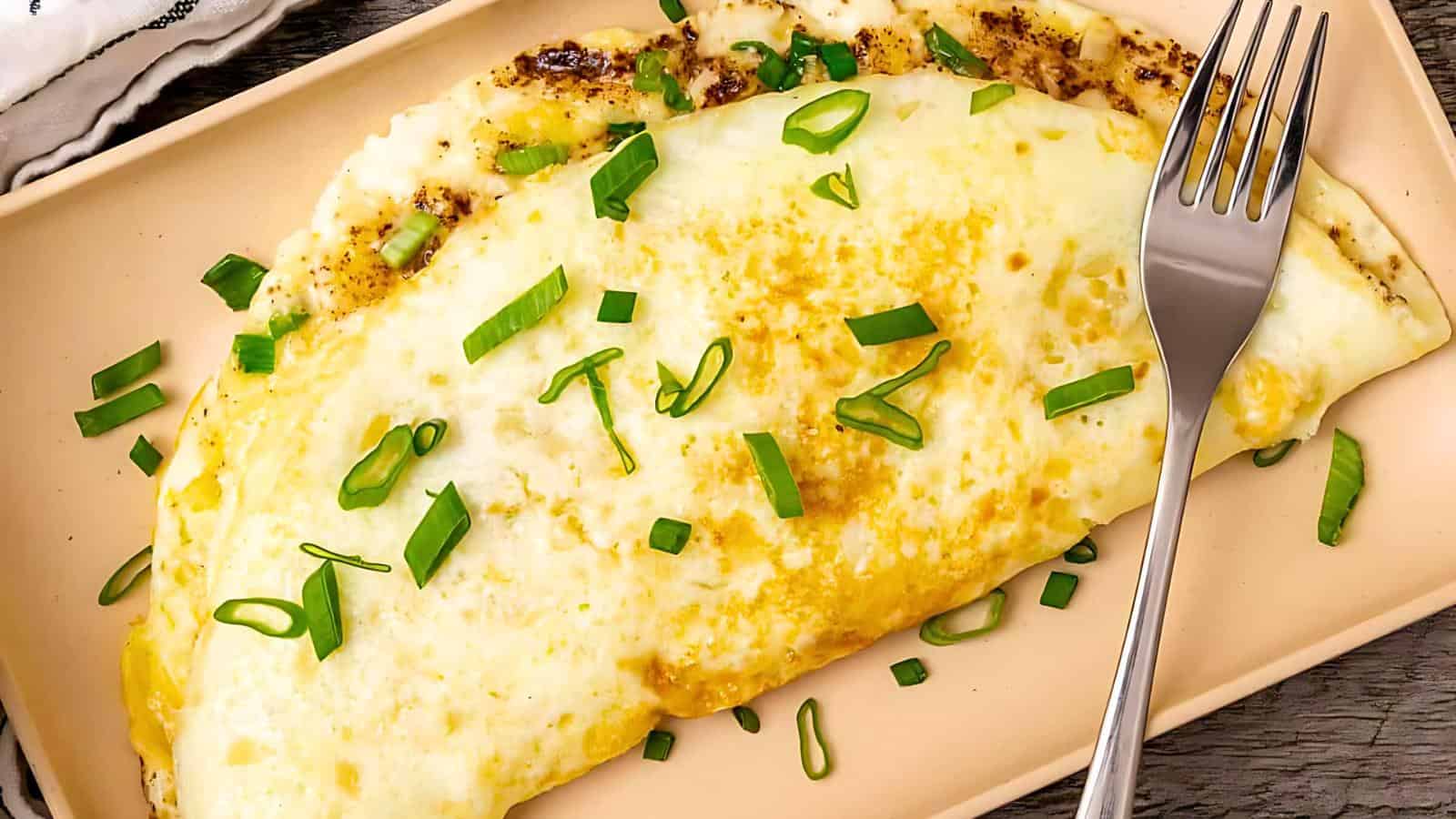 A folded omelet garnished with chopped green onions on a rectangular beige plate, with a fork placed beside it.