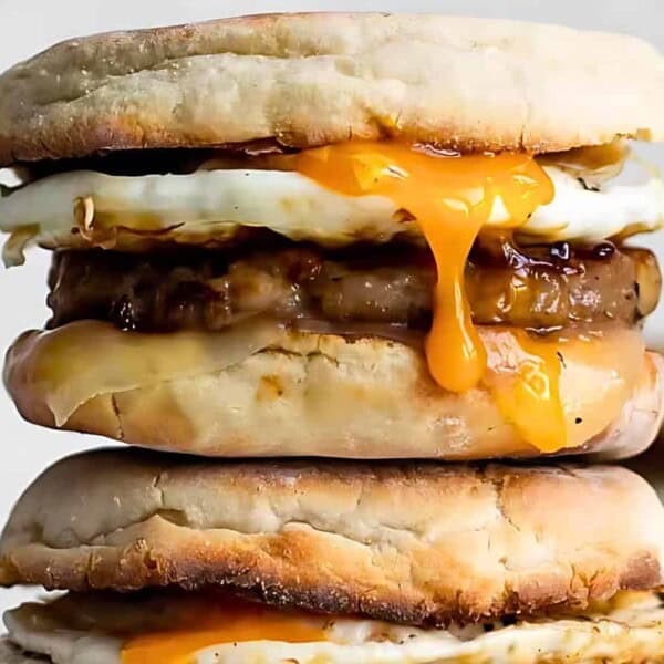 A stacked sandwich with fried eggs with runny yolks, cheese, and sausage patties.