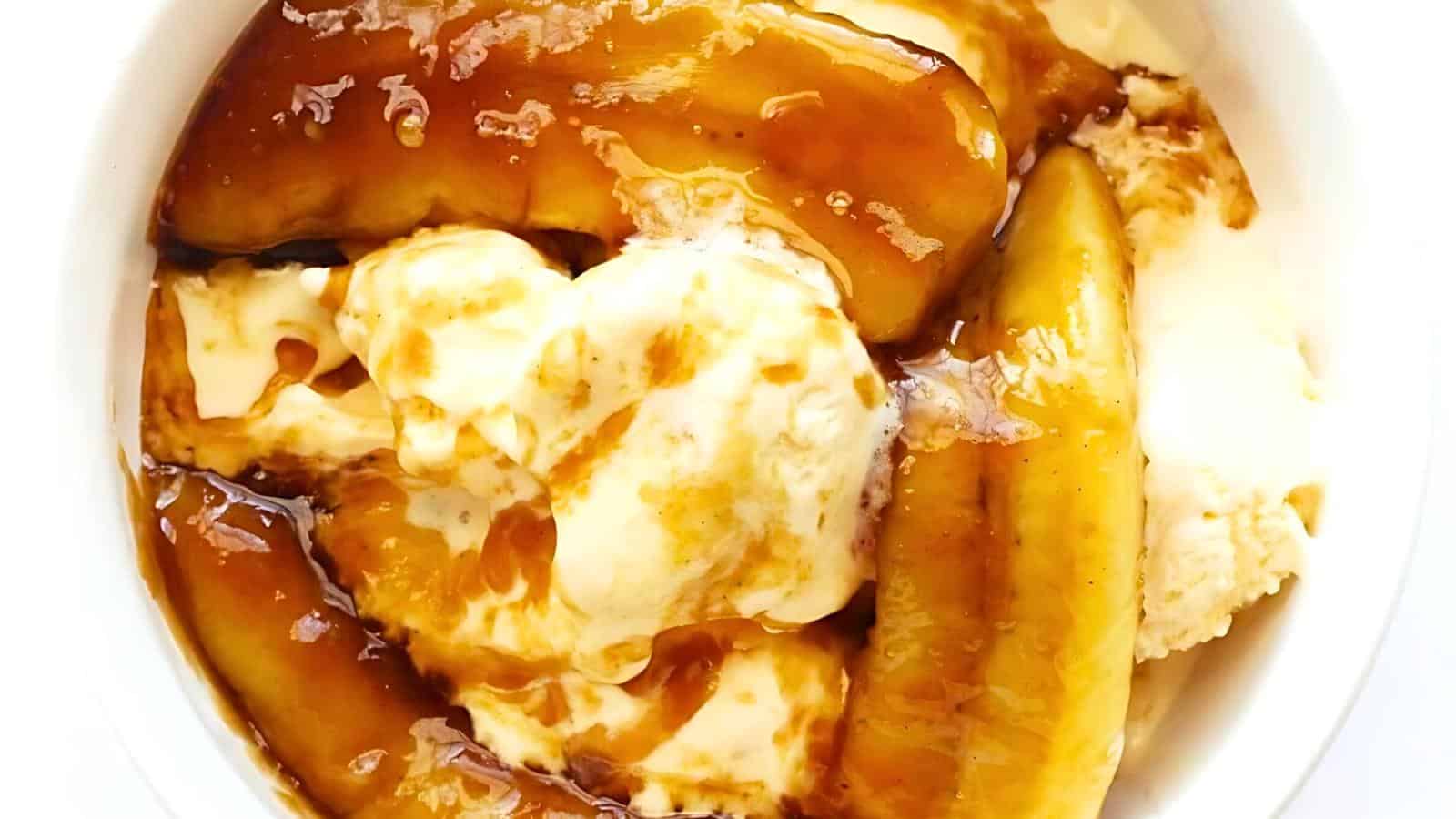 A bowl of caramelized bananas served over creamy vanilla ice cream. The bananas are golden brown and glossy with caramel sauce, creating a rich and indulgent dessert with a mix of warm bananas and cold, smooth ice cream.