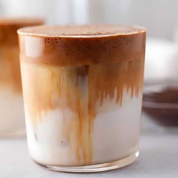 A glass of Dalgona coffee with whipped coffee foam on top, served over milk, and another glass in the background.