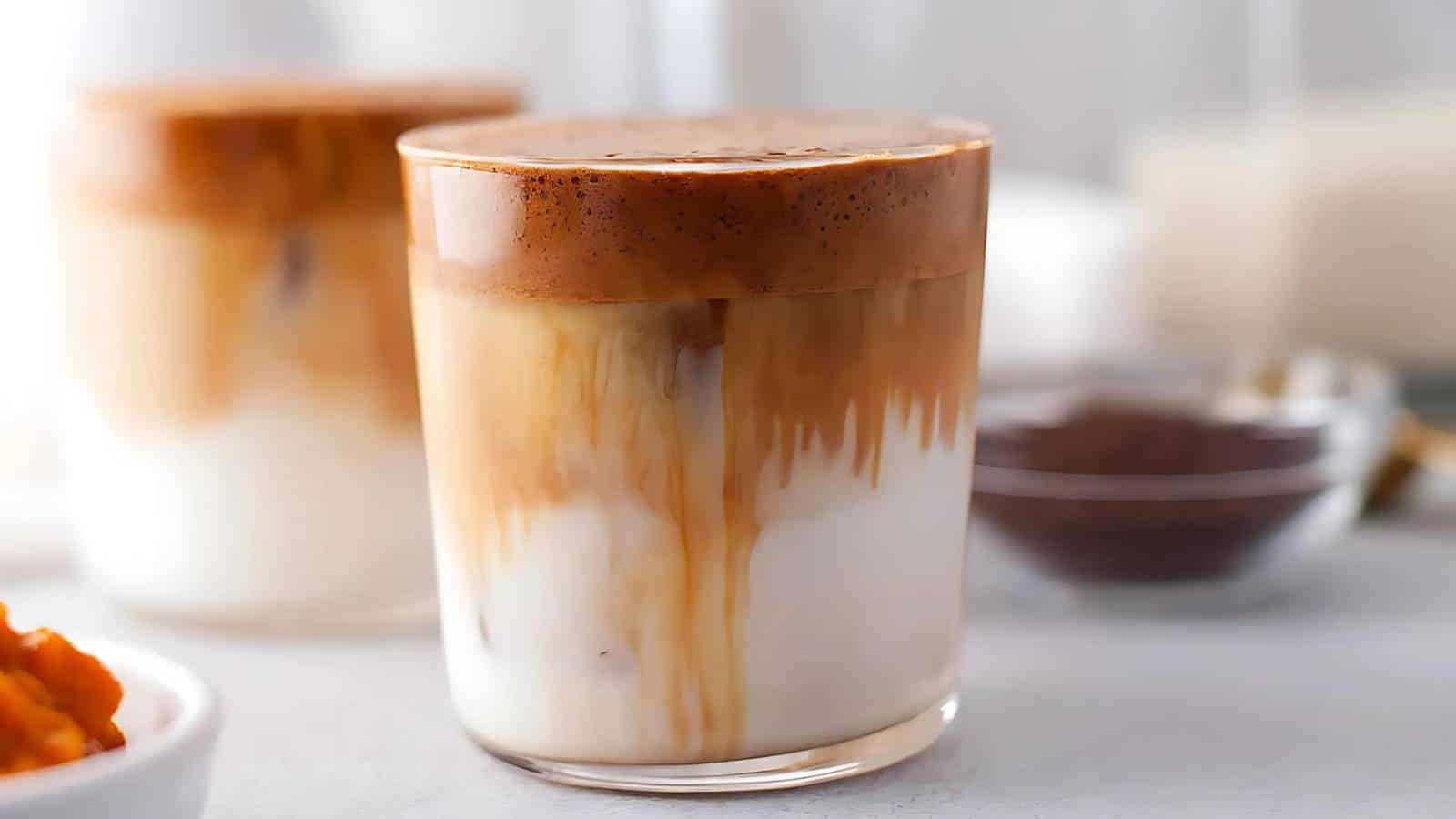 A glass of Dalgona coffee with whipped coffee foam on top, served over milk, and another glass in the background.