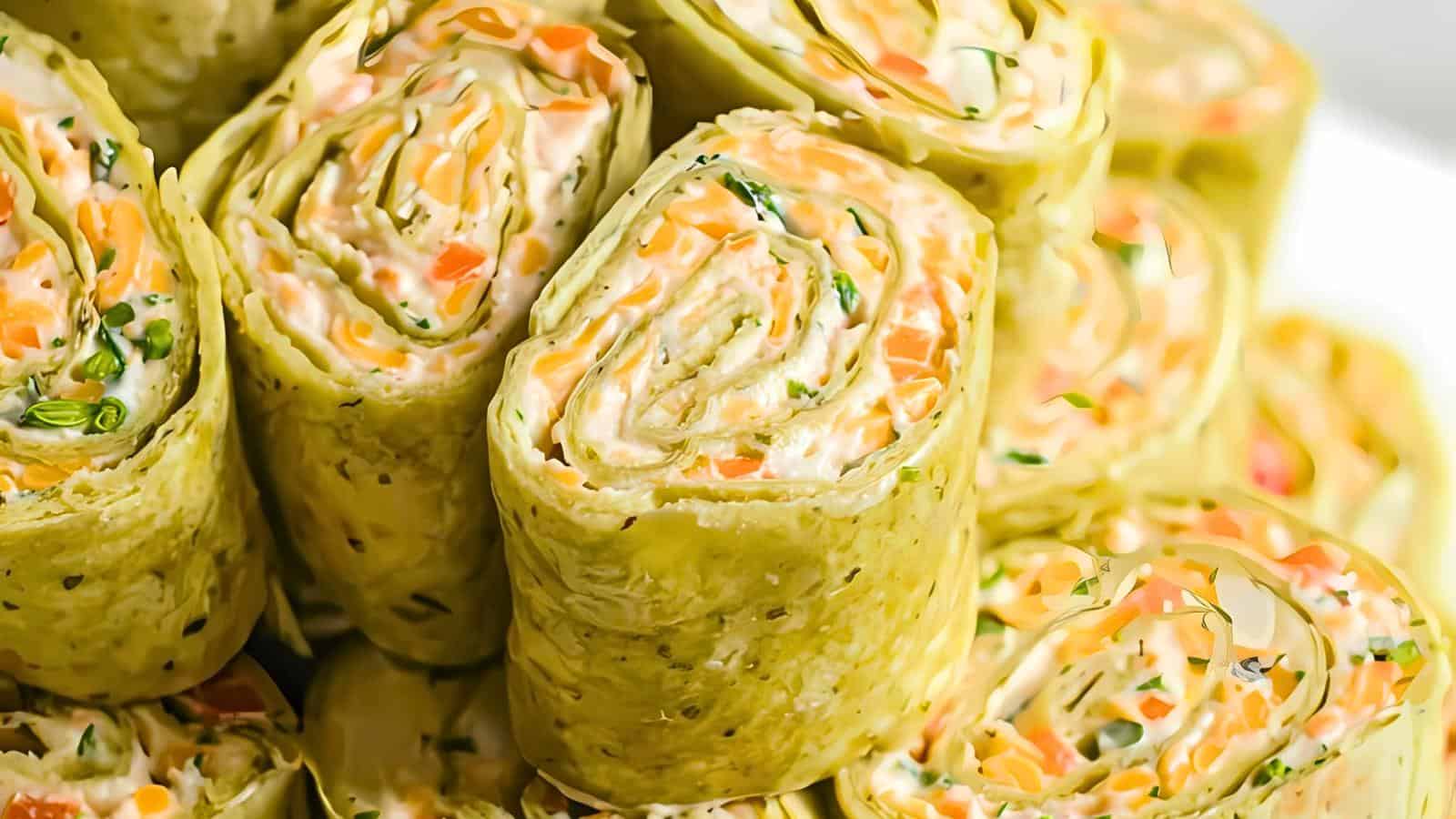 Close-up of multiple rolled tortillas filled with cream cheese, shredded vegetables, and herbs, neatly stacked.
