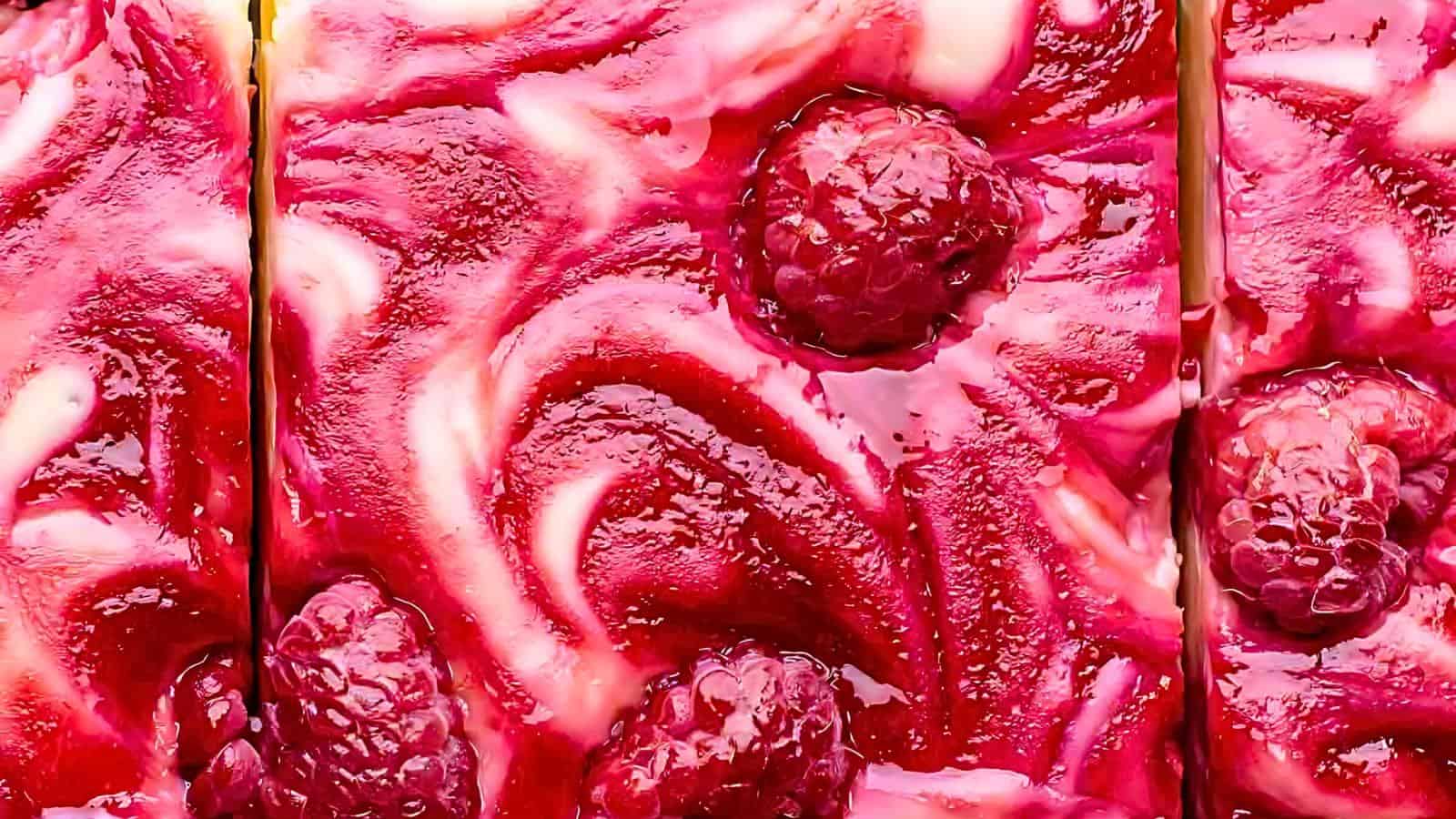 A raspberry cheesecake bar featuring a swirl of raspberry jam and topped with whole raspberries.