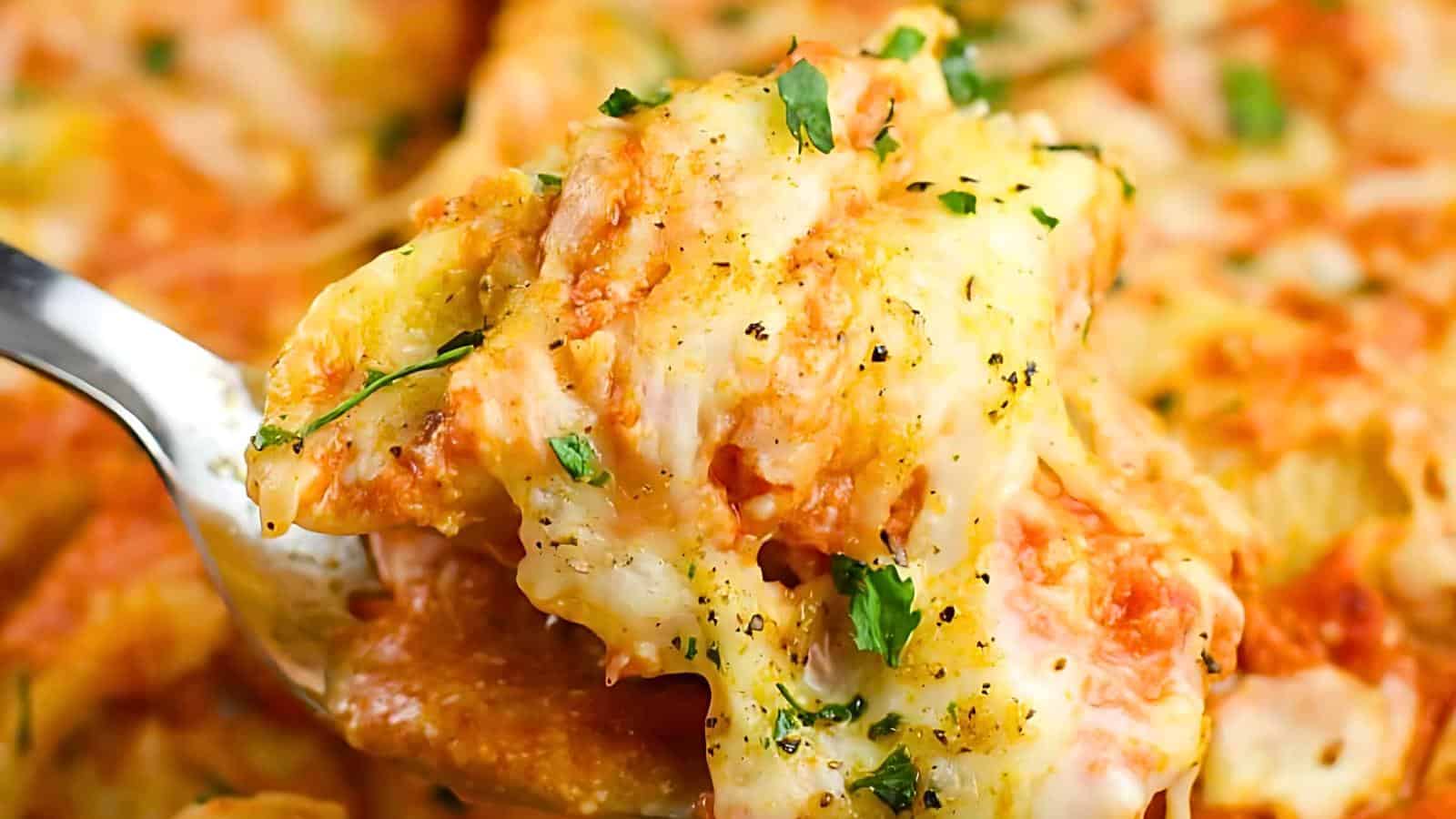 A fork lifting a cheesy, baked stuffed shells adorned with herbs.