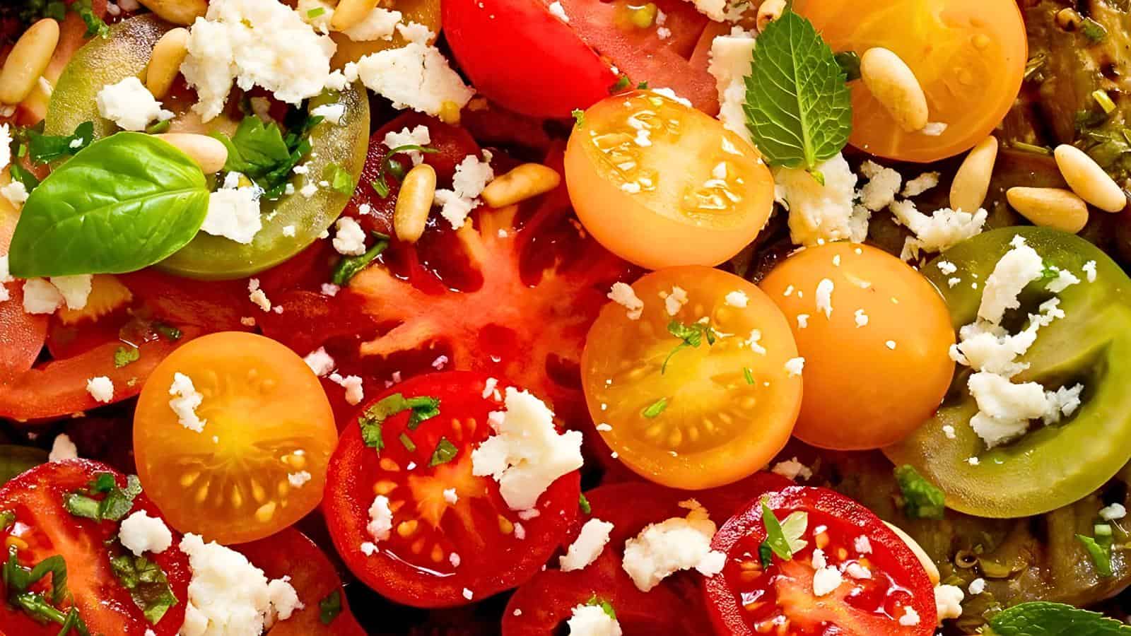 A fresh salad with colorful sliced tomatoes, crumbled cheese, pine nuts, basil, and mint leaves.