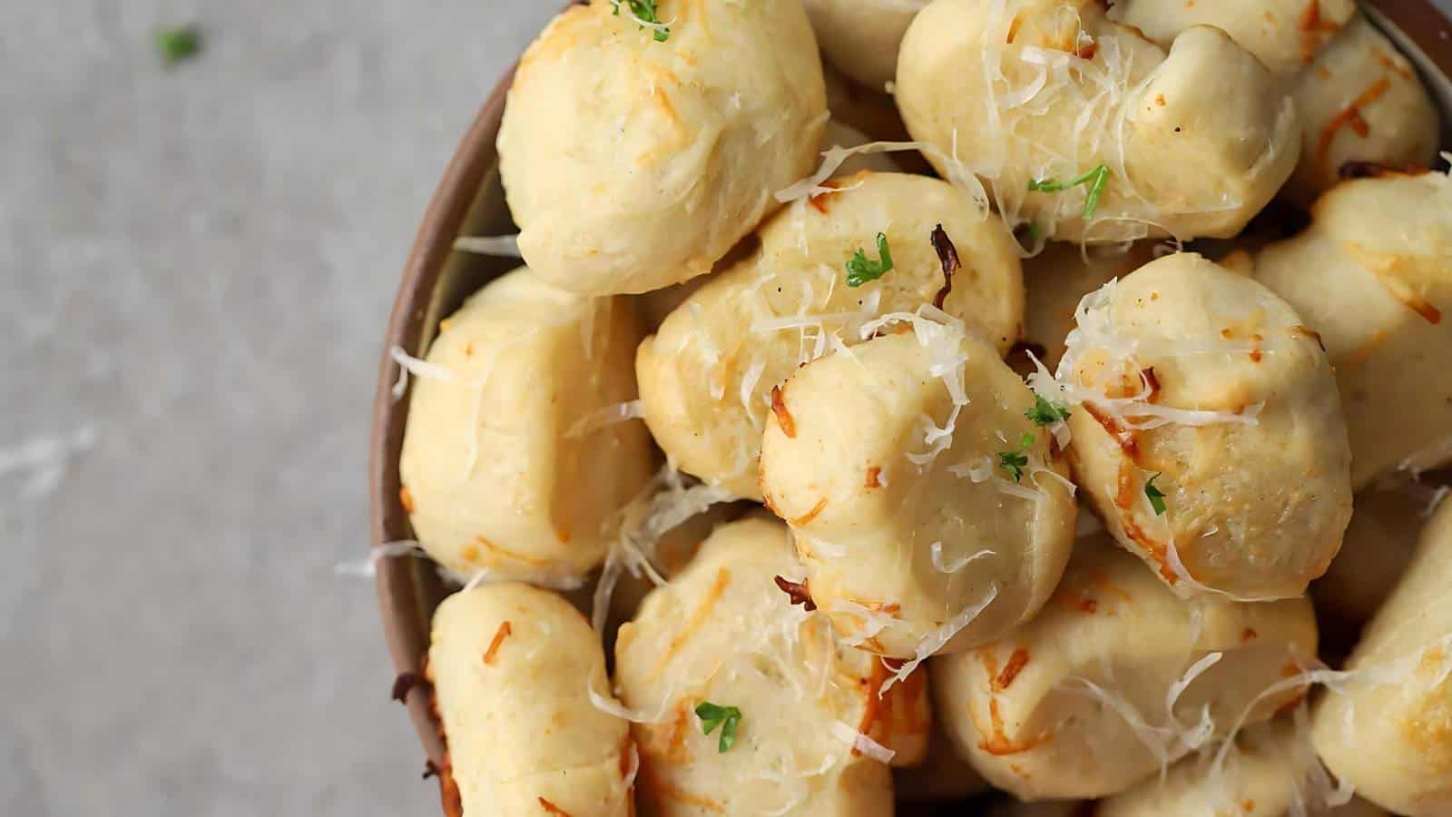A bowl of garlic knots topped with grated cheese and chopped parsley.