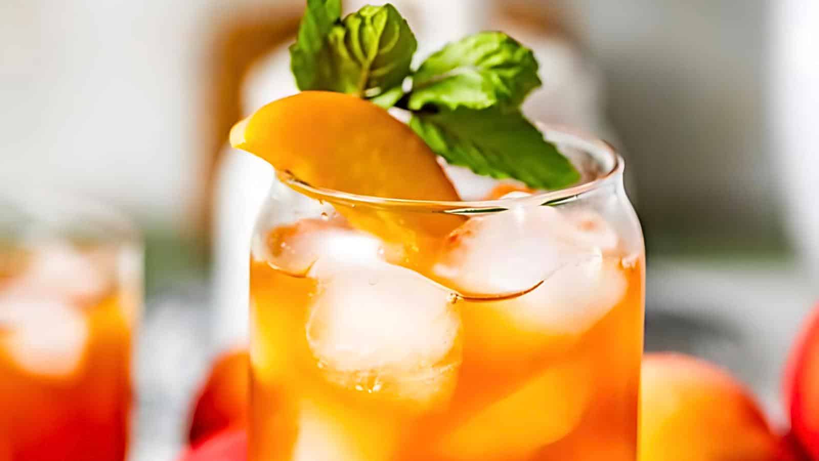 A glass filled with iced tea, garnished with a peach slice and a sprig of mint.