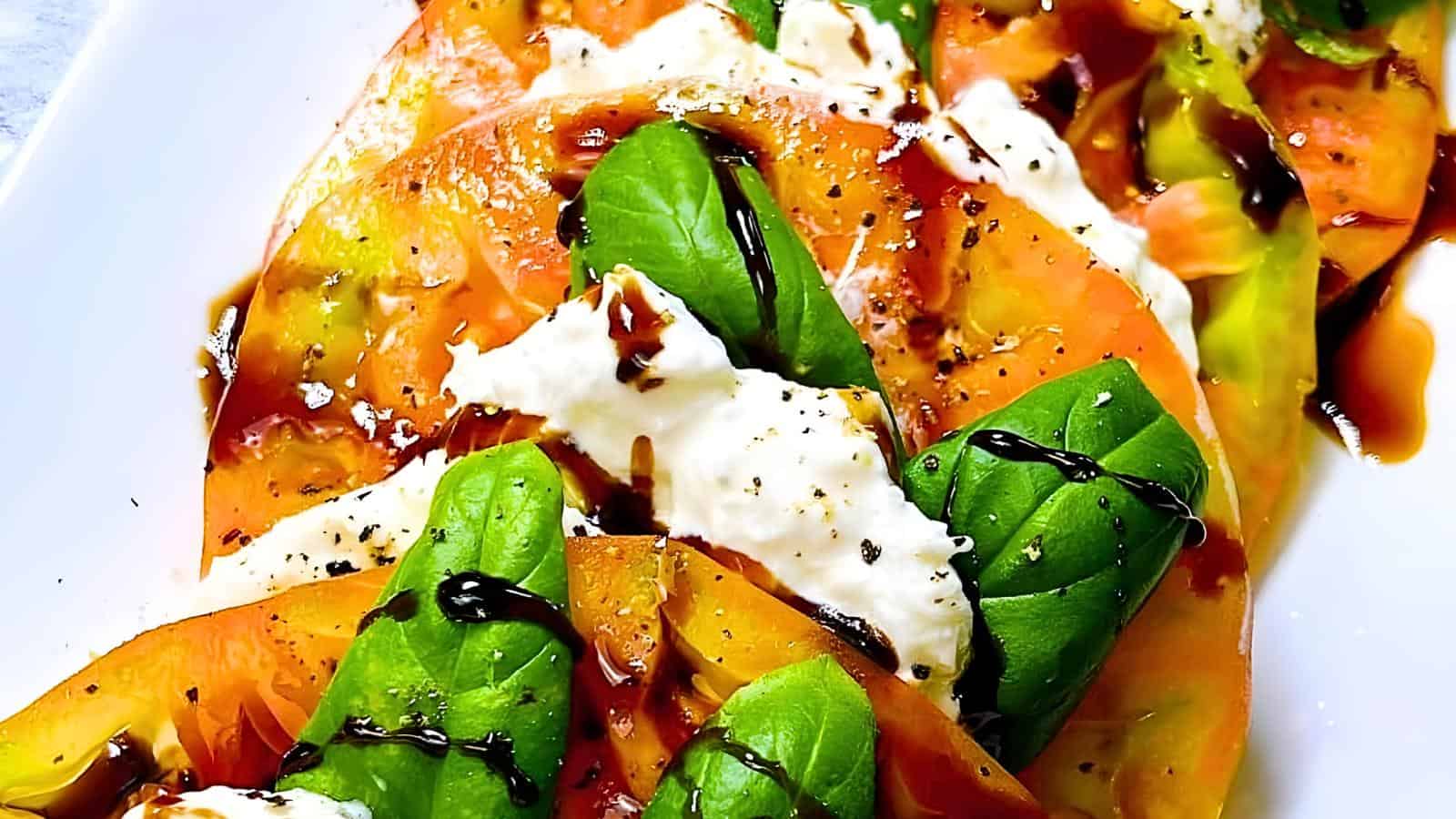 Slices of yellow tomato, fresh mozzarella, basil leaves, drizzled with balsamic glaze on a white plate.