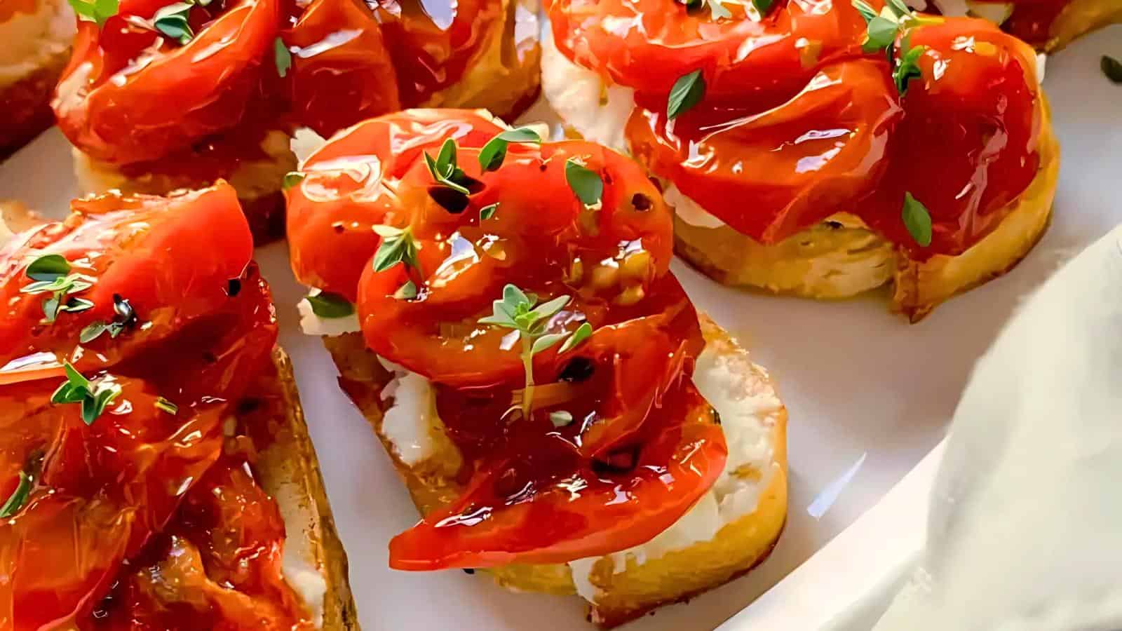 Close-up of toast topped with creamy cheese, roasted red tomatoes, and garnished with fresh herbs on a white plate.