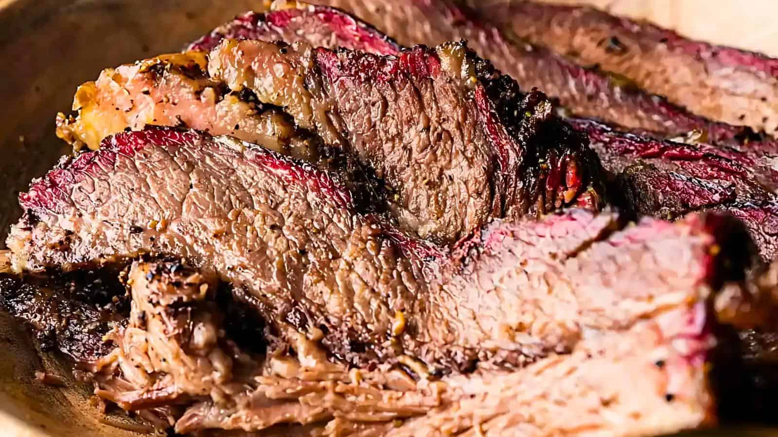 Sliced, cooked beef brisket with a charred exterior and marbled texture, featuring a reddish-brown crust and a moist interior, served on a wooden surface.