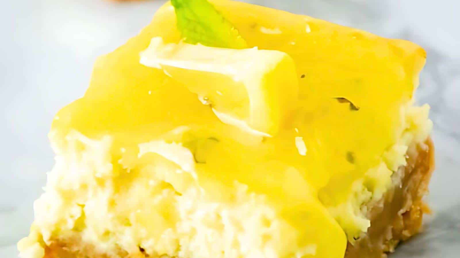 A lemon cheesecake topped with a slice of lemon and a green leaf on a marble surface.