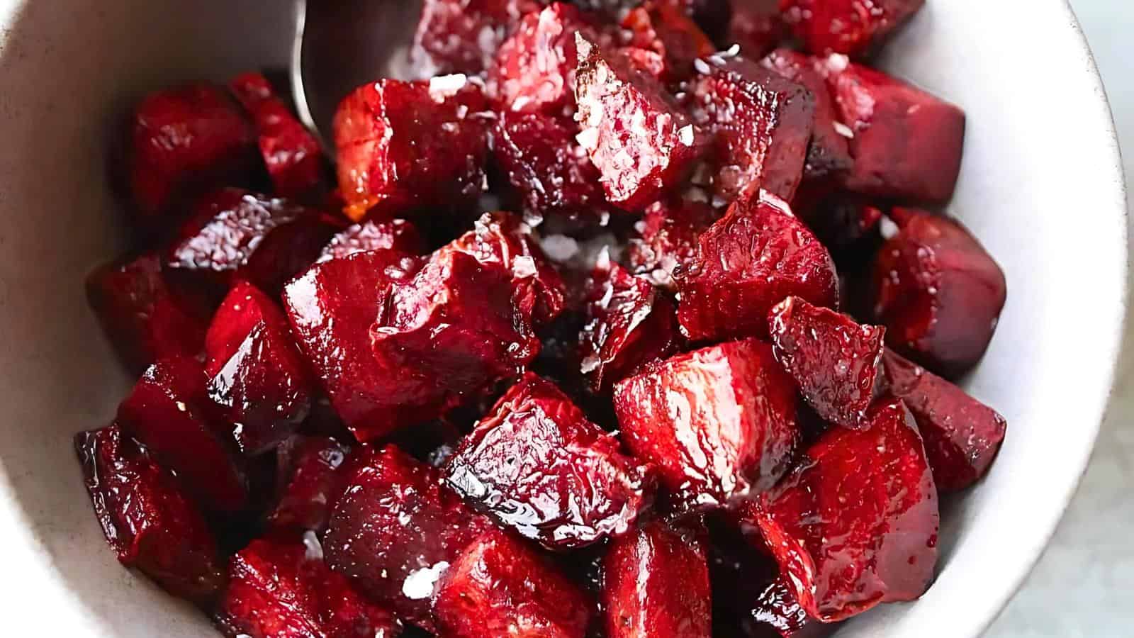 A bowl of roasted beetroot chunks, glistening with oil and seasoning, with a spoon partially visible in the background.