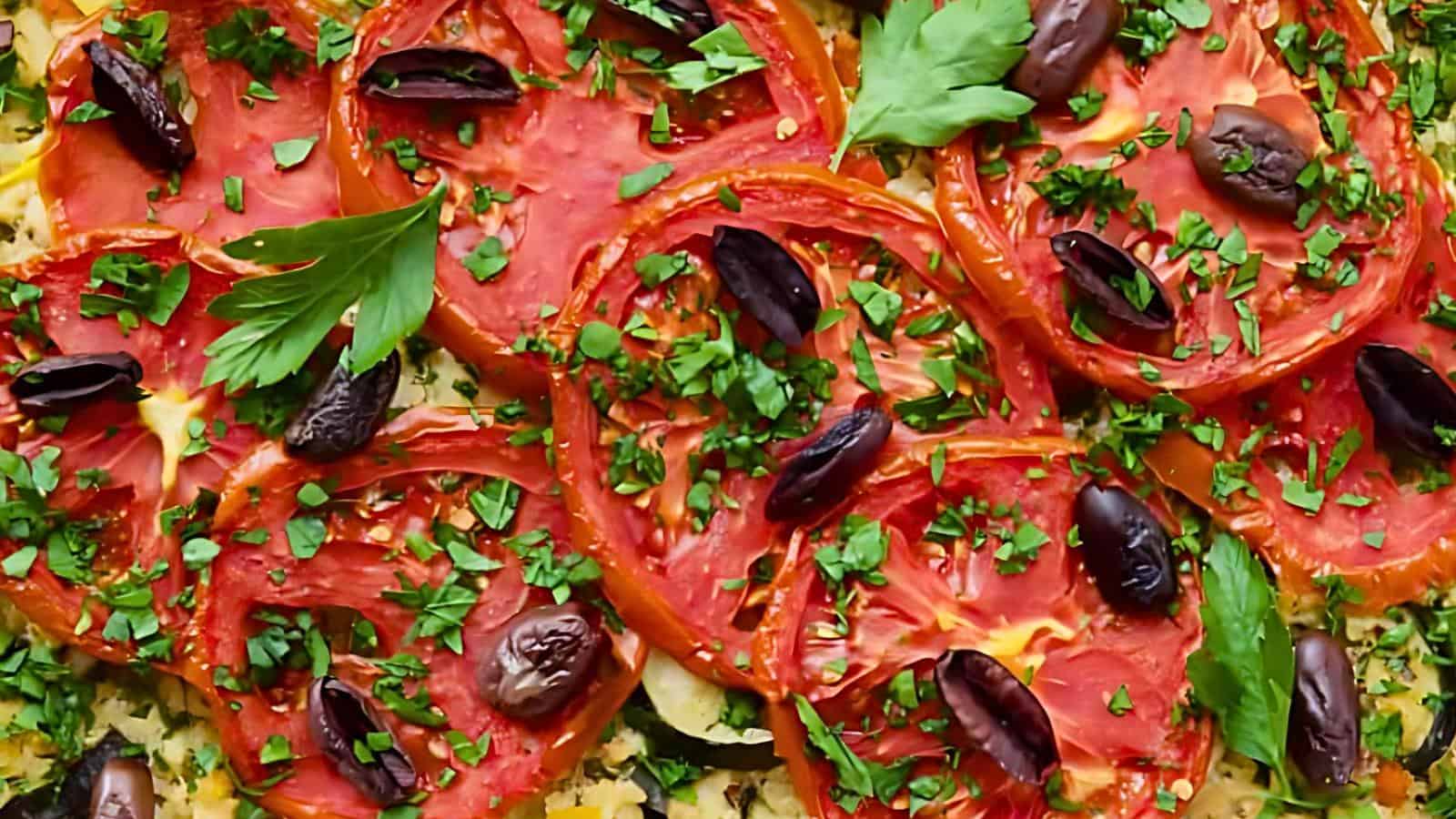 Sliced tomatoes topped with chopped parsley, black olives, and scattered fresh herbs.