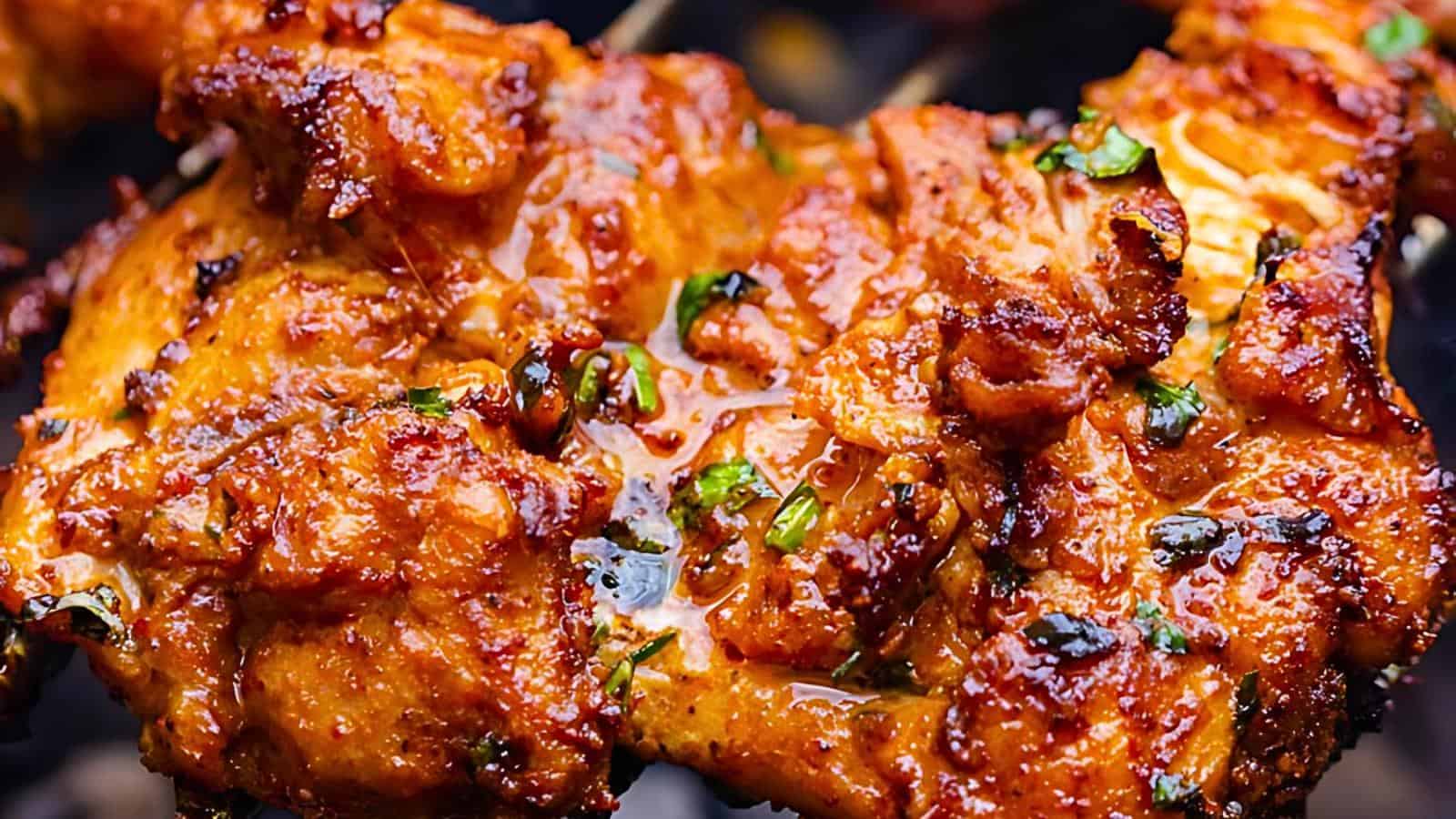 Sizzling, grilled meat with a golden-brown, crispy exterior garnished with chopped herbs.