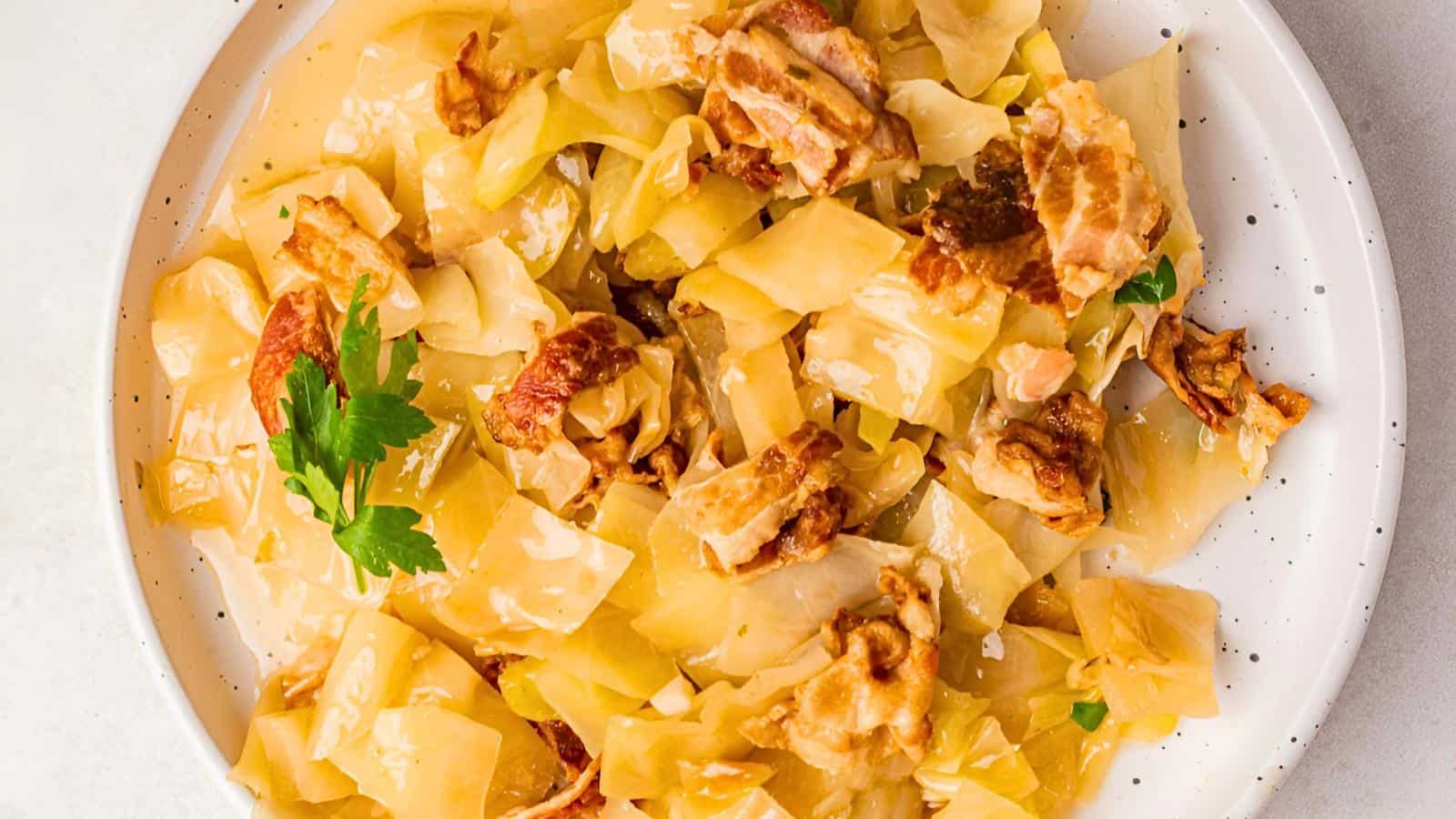 A plate of cooked cabbage and bacon pieces, garnished with a sprig of parsley.
