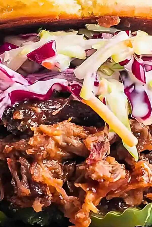 Close-up image of a smoked brisket sandwich with coleslaw and pickles on a bun.
