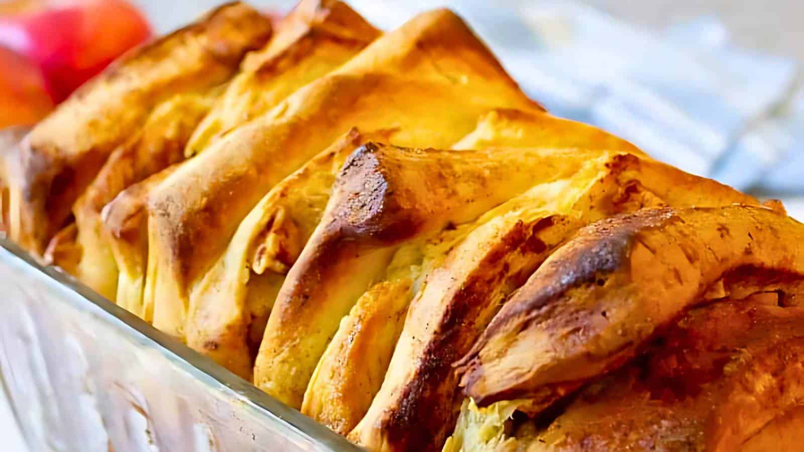Close-up of a freshly baked pull-apart bread with golden brown, flaky layers in a clear glass loaf pan.