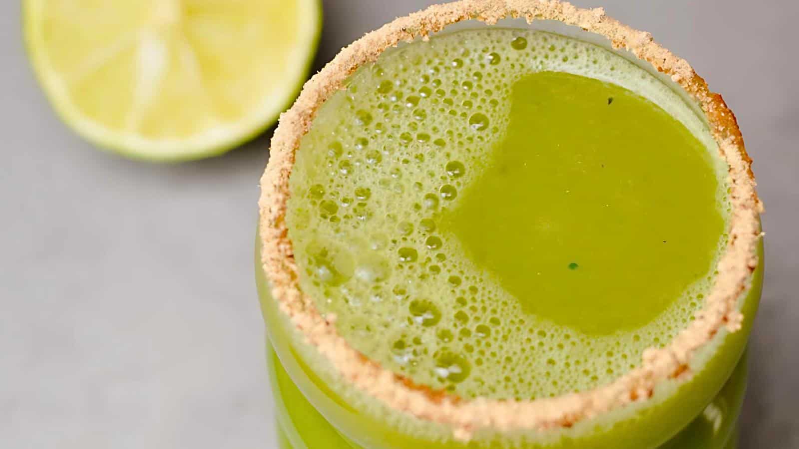 A green beverage in a glass with a crumb-coated rim and a halved lime in the background.