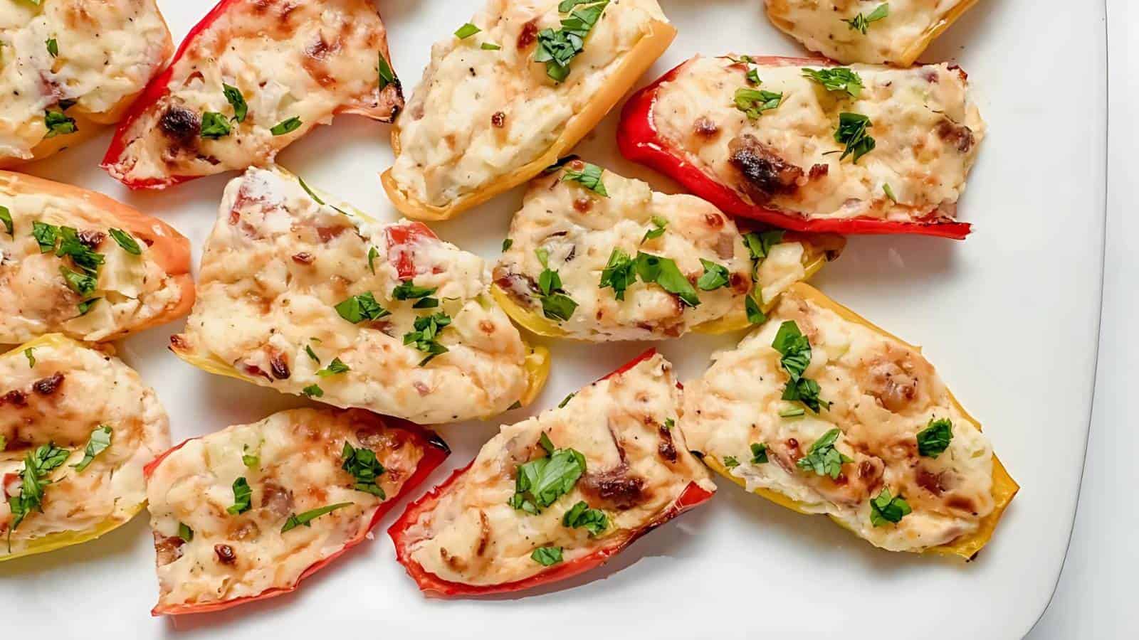 Colorful mini sweet peppers halved and filled with a creamy cheese mixture, garnished with chopped fresh herbs, arranged on a white plate.