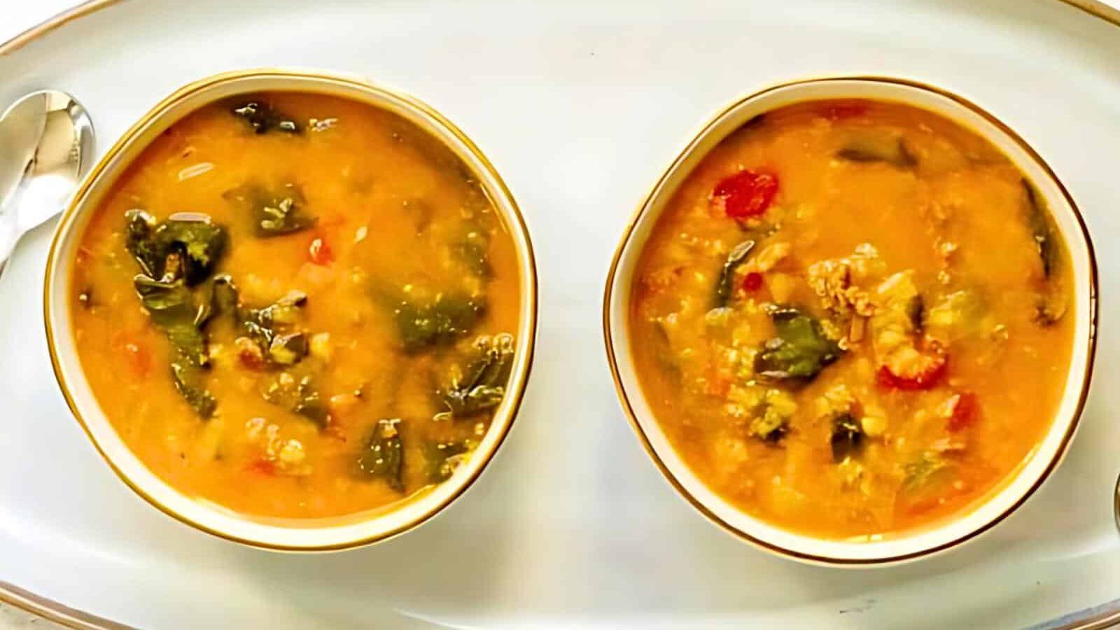 Two bowls of chunky vegetable stew and a spoon on a white tray.