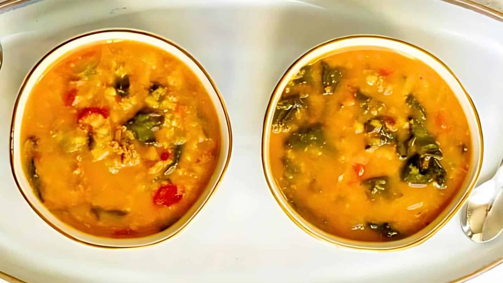 Two bowls of chunky vegetable stew and a spoon on a white tray.