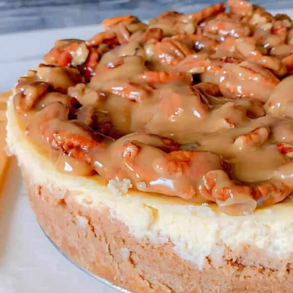 A cheesecake topped with caramel and pecans, next to an orange cloth napkin.