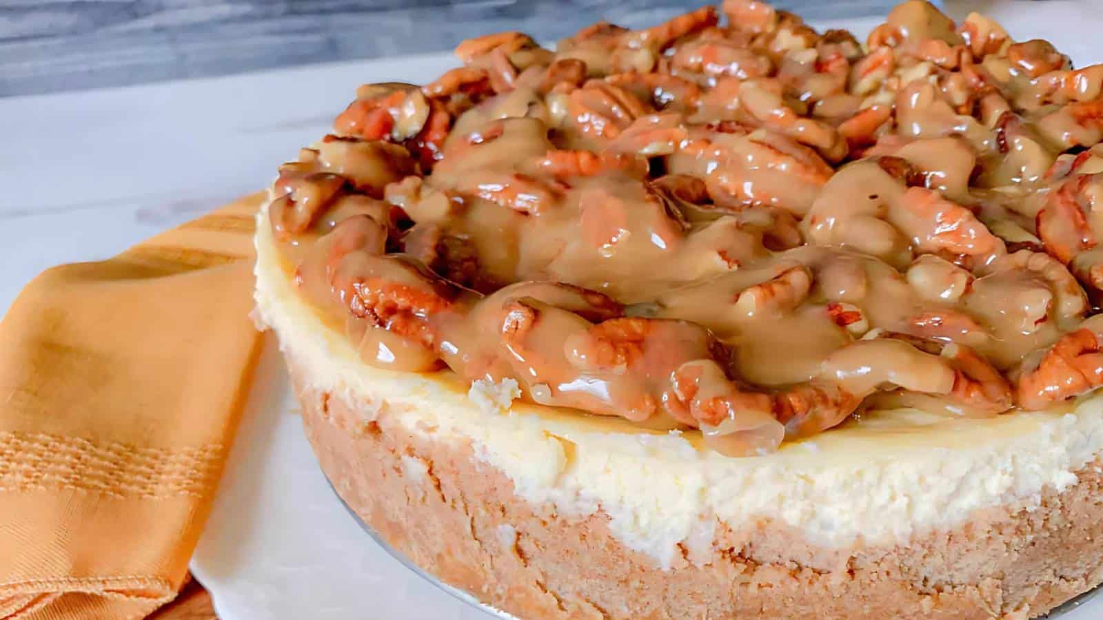 A cheesecake topped with caramel and pecans, next to an orange cloth napkin.