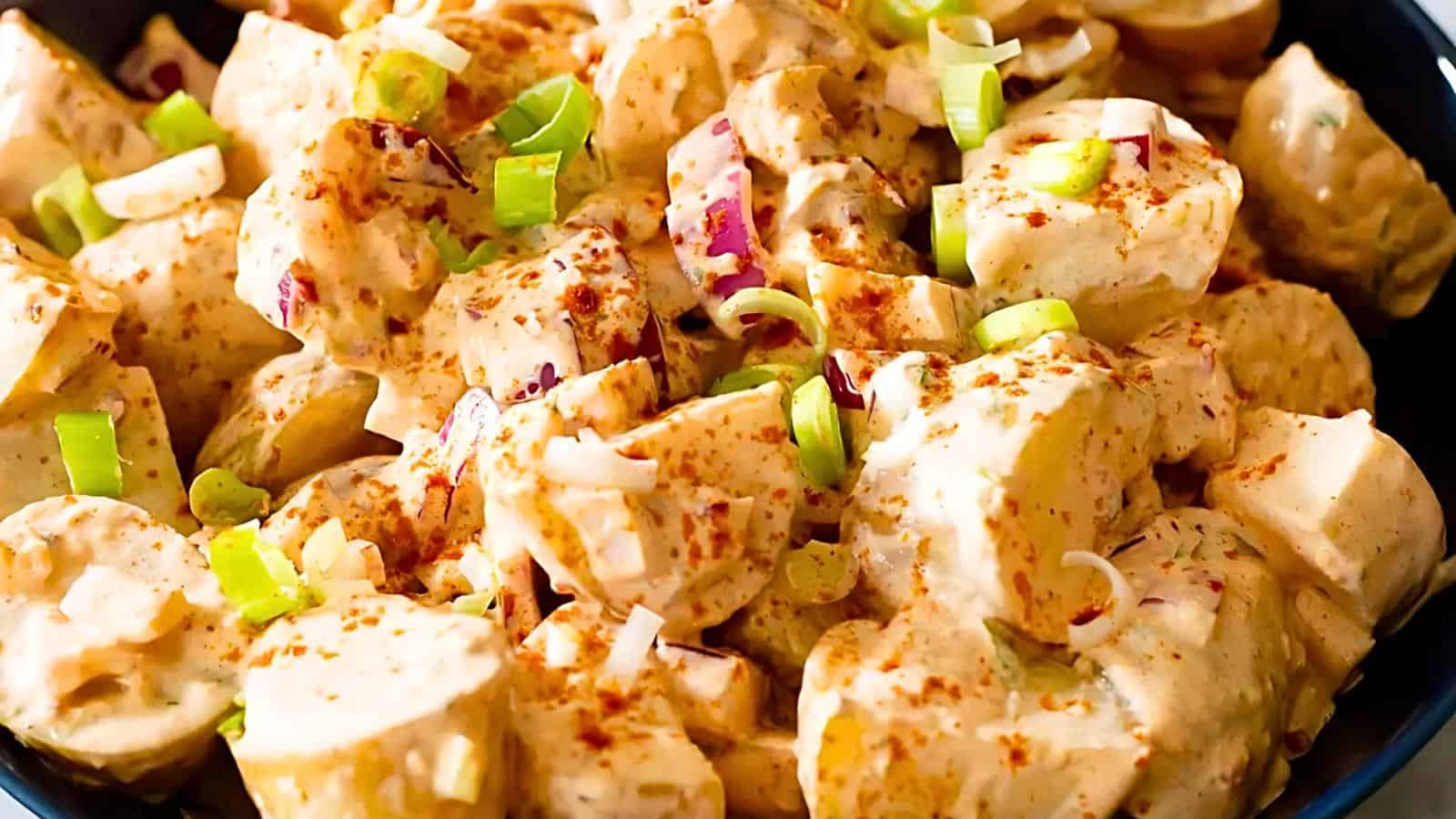 A plate of creamy potato salad with chopped green onions and a sprinkle of paprika.