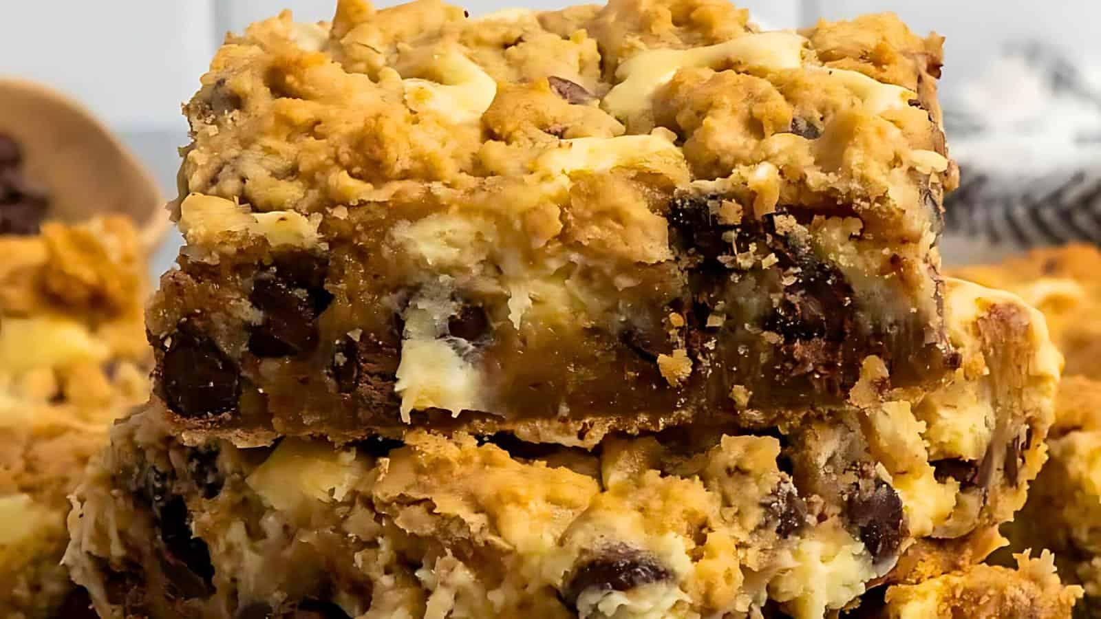 Two stacked dessert bars filled with chunks of chocolate and a creamy filling, showcasing a crumbly texture.