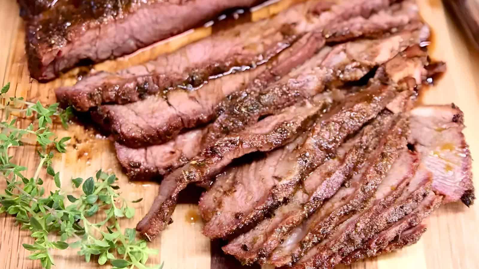 Slices of cooked brisket are displayed on a wooden cutting board, garnished with sprigs of fresh thyme.