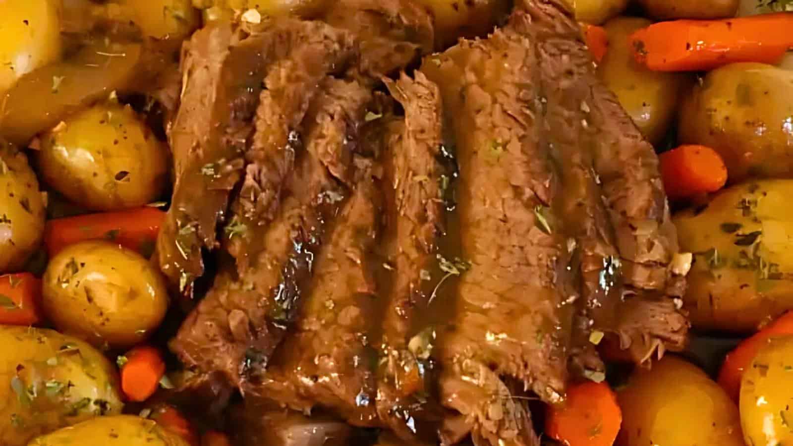 Sliced pot roast surrounded by baby potatoes and carrots, all covered in seasoning and gravy.
