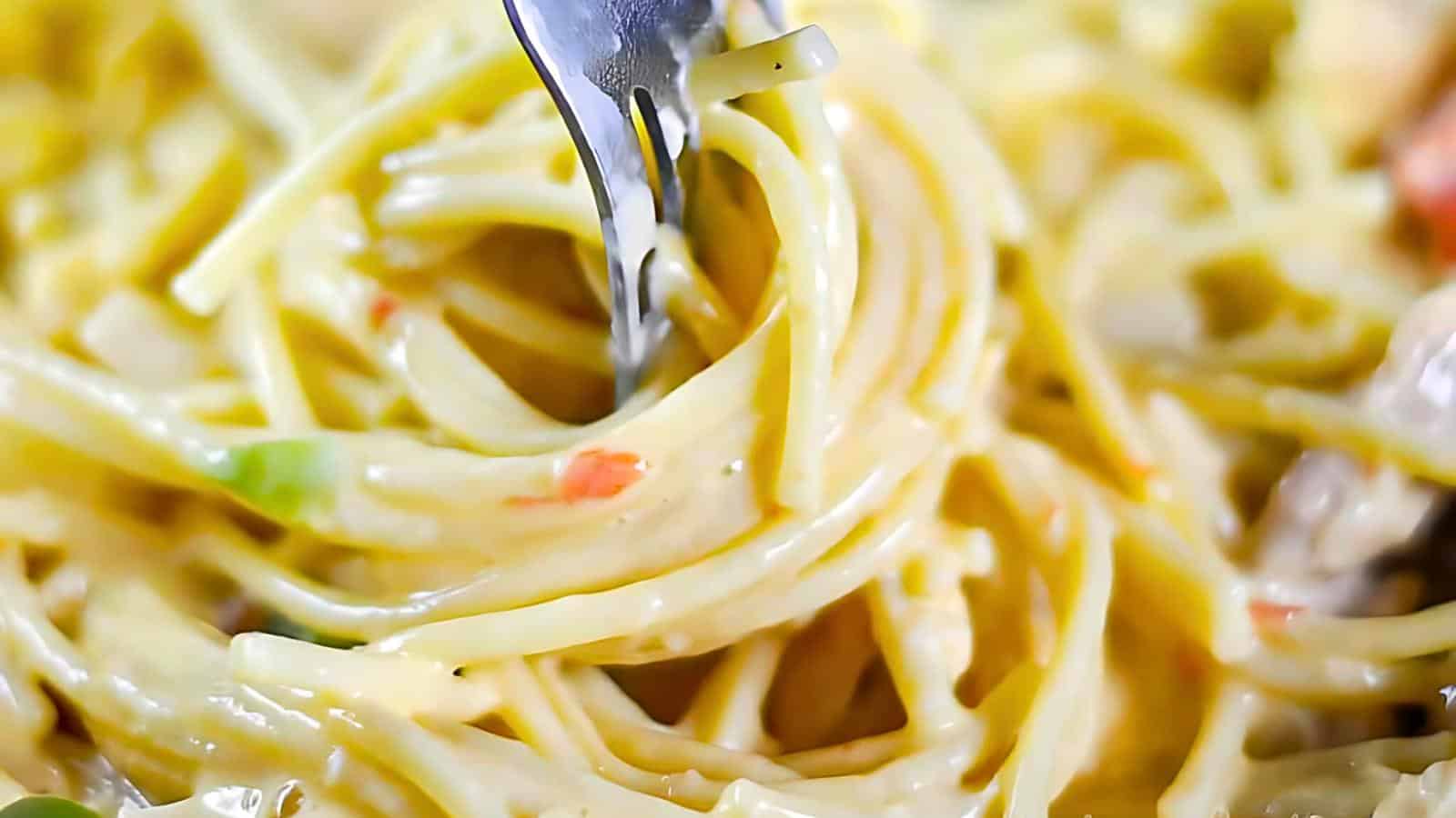 Fork twirling creamy pasta with visible bits of vegetables.