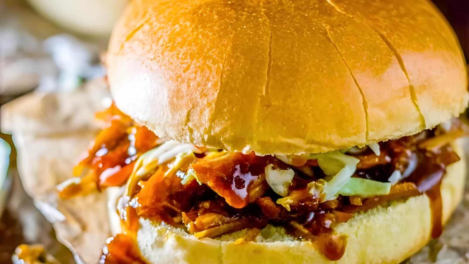 A close-up of a barbecue pulled pork sandwich with coleslaw in a bun.